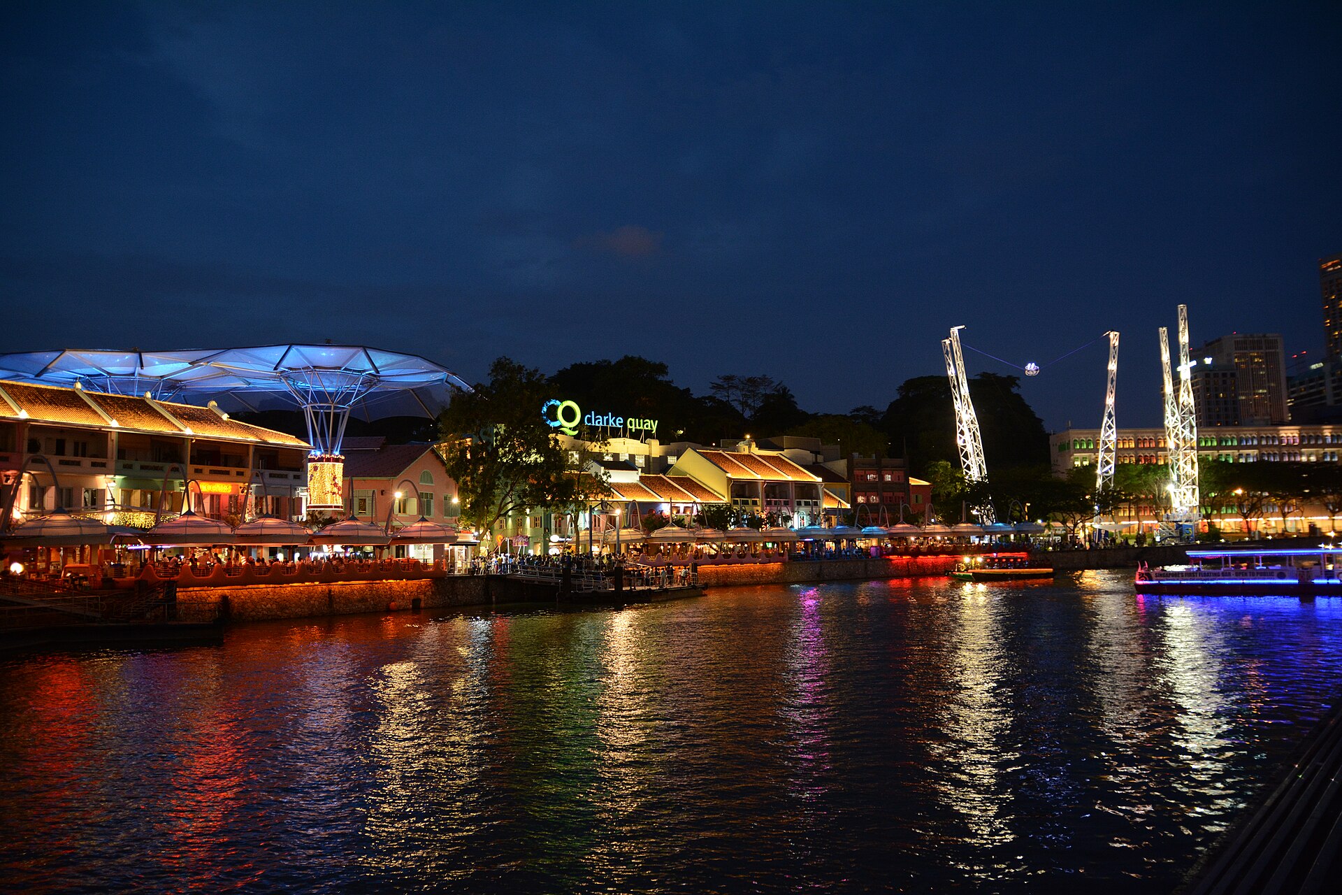 The lit shophouses and riverside restaurants of Clarke Quay reflected in the Singapore River at night