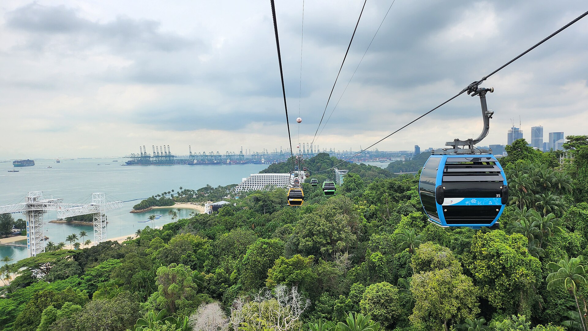 Cable car cabins above the forest of Sentosa, with Siloso beach and the harbour below